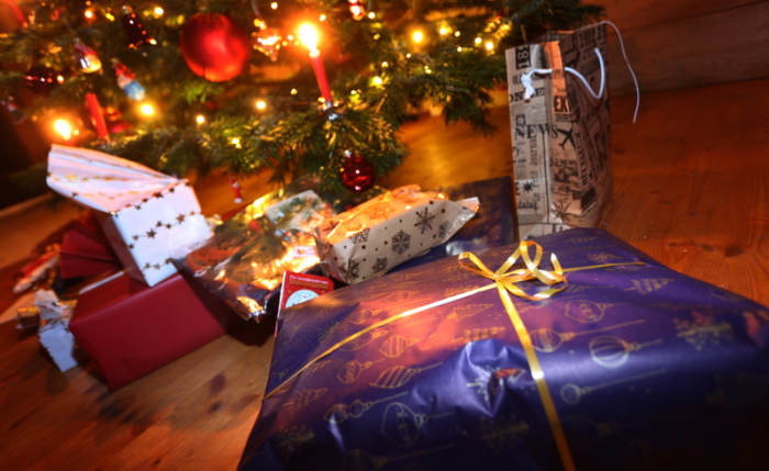Verpackte Geschenke liegen in einem Wohnzimmer unter einem festlich geschmücktem Weihnachtsbaum. Foto: Karl-Josef Hildenbrand/dpa