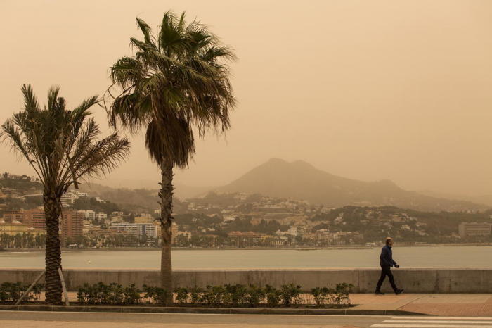 Ein Spaziergänger geht an der Hafenpromenade entlang, während Staub aus der Wüste Sahara in Málaga aufgewirbelt wird. Foto: epa/Daniel Perez