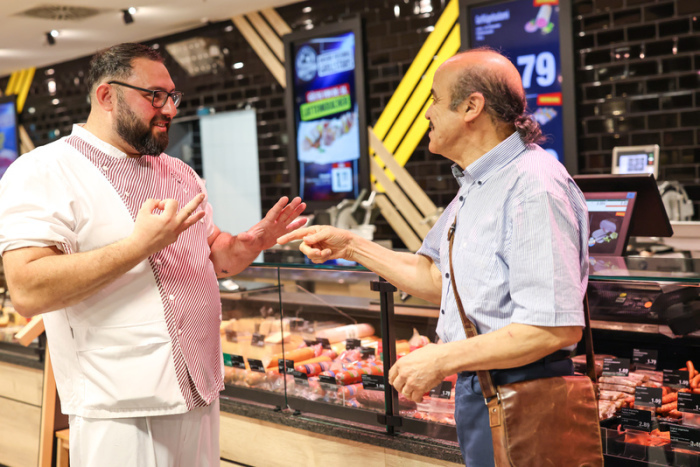 Metzger Yevgeniy Klibanov unterhält sich mithilfe von Gebärdensprache mit seinem gehörlosen Stammkunden Hedi Doudeche an der Supermarkt-Theke. Foto: dpa/Daniel Löb