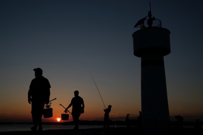 Fischer laufen bei Sonnenuntergang nahe des Bosporus in Istanbul entlang eines Leuchtturms während der Corona-Pandemie. Foto: epa/Sedat Suna