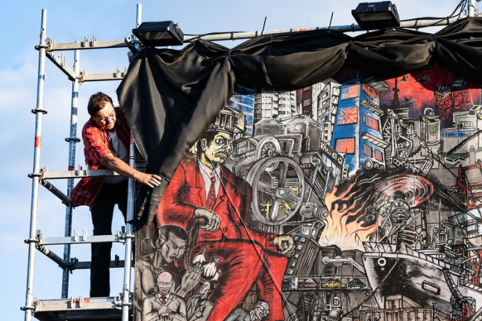 Ein Mitarbeiter der documenta fifteen verhüllt ein großflächiges Banner, eine Figurendarstellung 