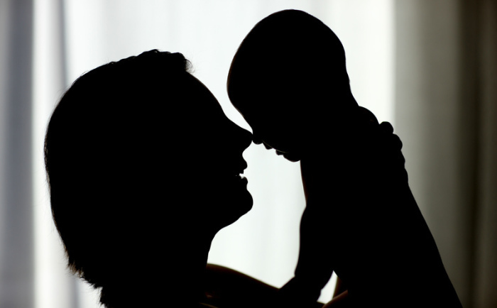 Eine Mutter hält ihr Baby hoch. Mütter mit Corona-Infektion sollten ihre neugeborenen Babys stillen und mit ihnen kuscheln dürfen. Foto: Patrick Pleul/dpa