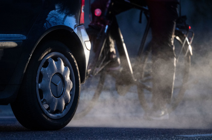 Ein Radfahrer steht neben einem Auto von Mercedes mit Dieselantrieb, dessen Abgase in der kalten Morgenluft sichtbar werden. Foto: Marijan Murat//dpa