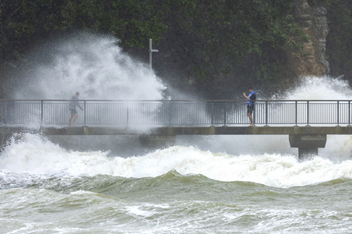 Menschen beobachten, wie Wellen gegen die Klippen eines Strandes schlagen. Foto: Brett Phibbs/Nz Herald/ap/dpa