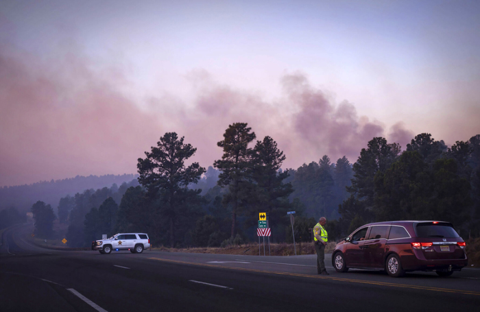 Der Rauch des South Fork Fire spiegelt bei Sonnenaufgang einen rosafarbenen Farbton wider, als Polizisten Autofahrer auf der State Road 48 an der State 220 wegen der Waldbrände in der Nähe von ... Foto: Chancey Bush/The Albuquerque Journal/ap/dpa