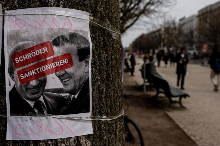 Ein Plakat, das den ehemaligen deutschen Bundeskanzler Gerhard Schröder mit einem Schild mit der Aufschrift 