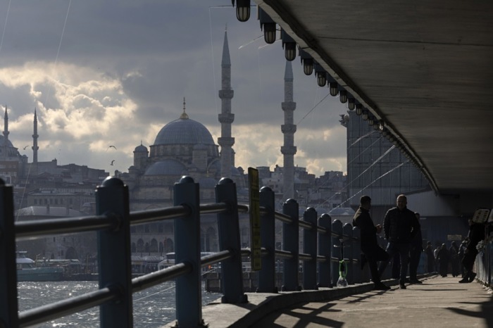 Menschen überqueren die Galata-Brücke in Istanbul am Goldenen Horn unter grauem Himmel und zeigen den Alltag der Stadt heute dort. Foto: epa/Tolga Bozoglu