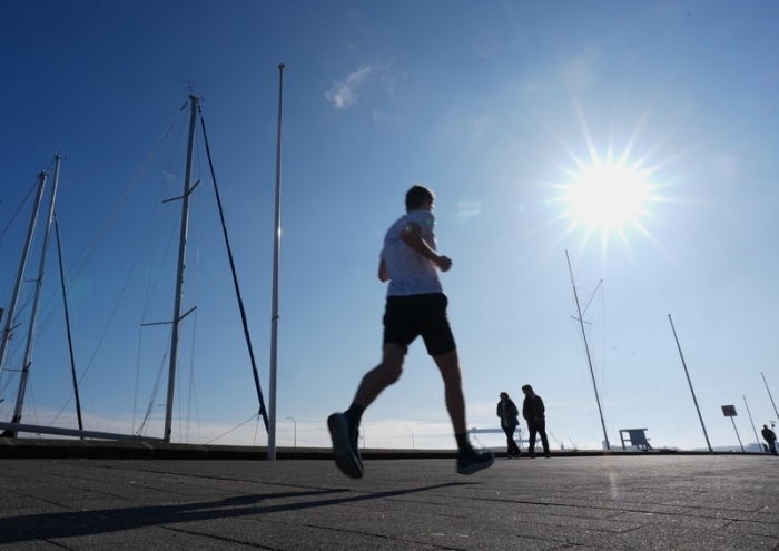 Ein Jogger läuft bei frühlingshaftem Wetter am Sportboothafen an der Kiellinie vorbei. Foto: Marcus Brandt/dpa