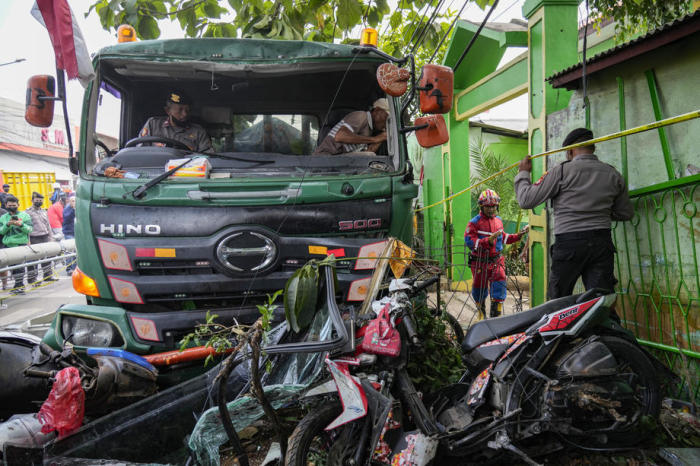 Rettungskräfte und Polizeibeamte untersuchen die Unfallstelle, nachdem ein Lkw einen Mobilfunkmast und eine Bushaltestelle vor einer Grundschule in Bekasi gerammt hat. Foto: epa/Str