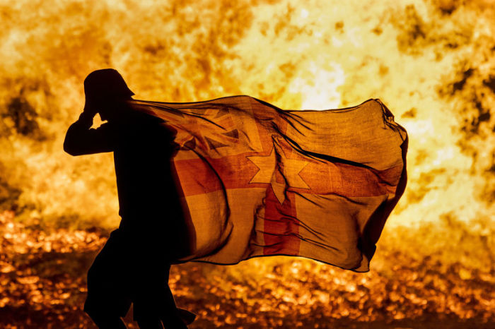 Ein junger Mann trägt eine nordirische Fahne am brennenden Craigyhill-Feuer der Loyalisten anlässlich der Feierlichkeiten zum Orangemen's Day. Archivfoto: Liam Mcburney/PA Wire/dpa