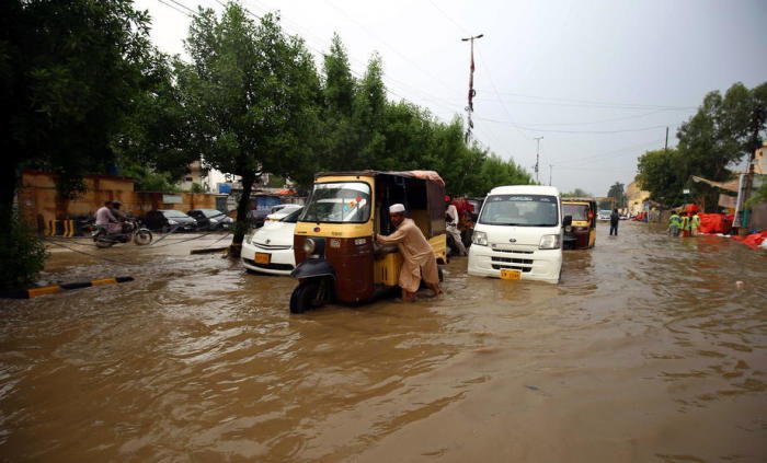 Nach schweren Regenfällen bahnen sich Menschen ihren Weg durch ein überschwemmtes Gebiet in Karachi. Foto: epa/Shahzaib Akber