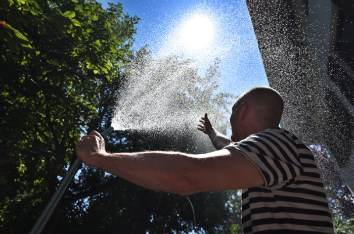 Ein Mann erfrischt sich in einem Garten mit Wasser aus einem Gartenschlauch. Foto: Karl-Josef Hildenbrand/dpa