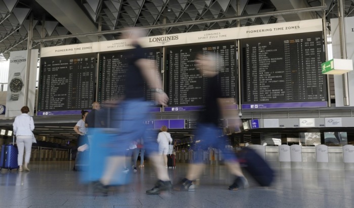 Reisende mit ihrem Gepäck bewegen sich in einem Abfertigungsgebäude mit einer Fluginformationstafel am internationalen Flughafen in Frankfurt am Main. Foto: epa/Ronald Wittek