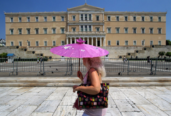Eine Frau hält einen Regenschirm vor dem griechischen Parlament in Athen, um sich vor der Sonne zu schützen. Foto: epa/Simela Pantzartzi