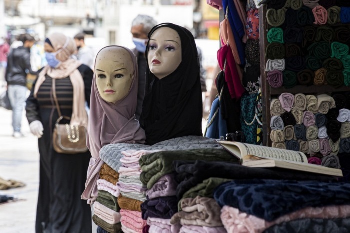 Eine Frau mit einer Schutzmaske geht in einem Textilgeschäft in der Innenstadt von Amman an Schaufensterpuppen mit Kopftüchern vorbei. Foto: epa/Andre Pain