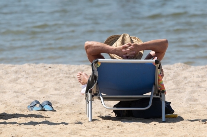 Ein Mann liegt mit einem Sonnenhut auf einer Sonnenliege am Ufer des Bärwalder See am Strand. Foto: Sebastian Kahnert/dpa-zentralbild/dpa
