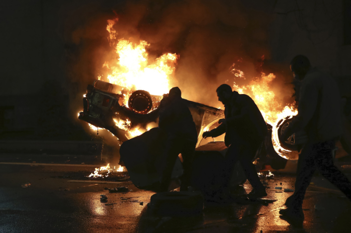Demonstranten bewegen einen Müllcontainer vor einem brennenden Polizeiauto unweit des georgischen Parlamentsgebäudes. Foto: Zurab Tsertsvadze/Ap