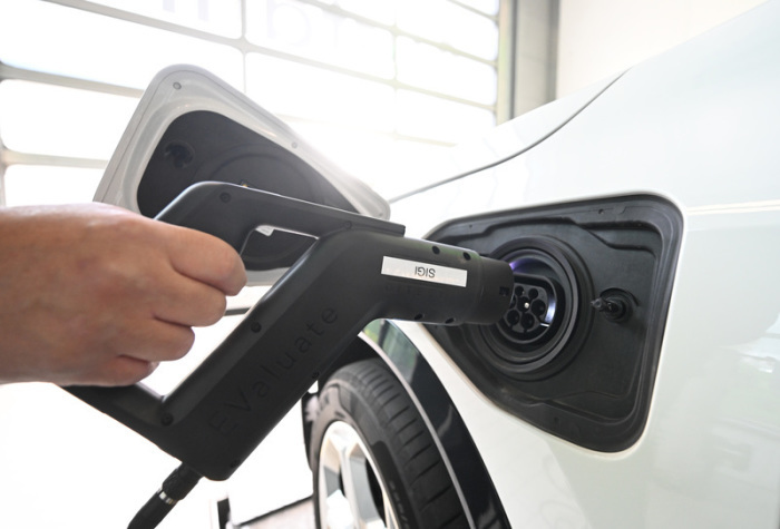 Ein Mitarbeiter lädt in einer Prüfhalle von Dekra in Stuttgart ein Elektroauto während einer technischen Untersuchung auf. Foto: Bernd Weißbrod/dpa