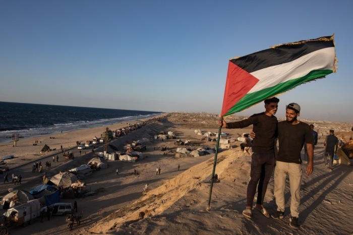 Zwei Männer mit palästinensischer Flagge begleiten Vertriebene, die entlang der Küstenstraße Al-Rashid in Richtung Gaza-Stadt ziehen. Foto: epa/Haitham Imad