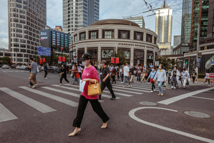 Leute gehen neben dem großen Bildschirm mit den neuesten Aktien- und Währungsdaten in Shanghai spazieren. Foto: epa/Alex Plavevski