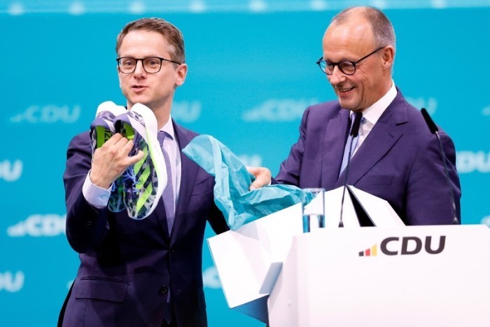 Carsten Linnemann (l), CDU Generalsekretär, hält Laufschuhe in der Hand, nachdem sie ihm von Friedrich Merz, CDU Bundesvorsitzender, beim CDU-Bundesparteitag überreicht wurden. Foto: Carsten Koall/dpa