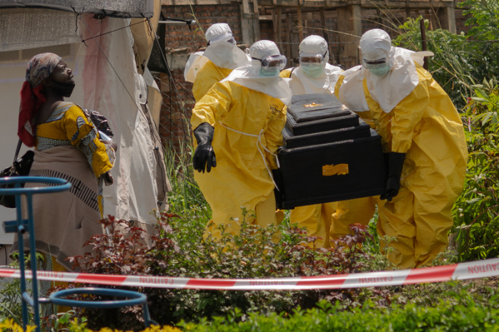 Eine Frau weint, als Mitarbeiter des Roten Kreuzes in Schutzanzügen den Sarg einer an Ebola verstorbenen Person aus einem Gesundheitszentrum in Rwampara tragen. Foto: Moses Sawasawa/Ap/dpa