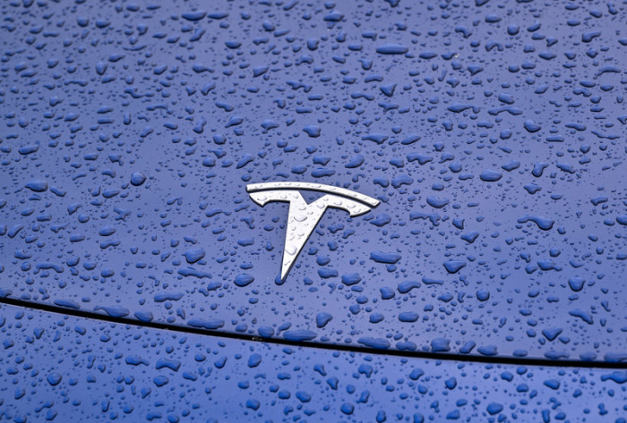 Regentropfen sind auf einem Pkw mit dem Tesla-Symbol vor dem Werk der Tesla-Autofabrik zu sehen. Foto: Patrick Pleul/dpa