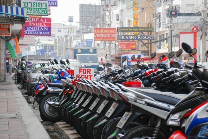 Motorräder zur Vermietung säumen eine Straße in einem thailändischen Touristengebiet. Branchenvertreter sehen mangelnde Kontrollen und illegale Angebote als wachsendes Problem für den Tourismussektor. Foto: polya_olya/Adobe Stock
