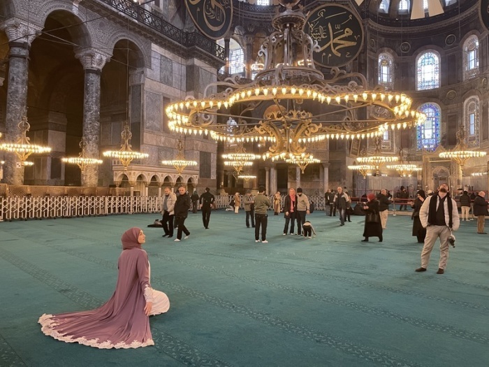 Eine Frau sitzt in der Hagia Sophia zwischen Betenden und Besuchern. Foto: Linda Say/dpa