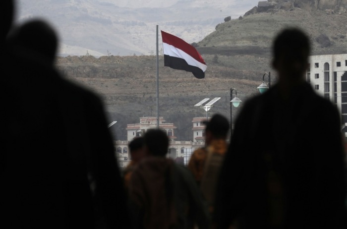 In Sana'a zeichnen sich Menschen vor einer wehenden jemenitischen Flagge ab. Foto: epa/Yahya Arhab