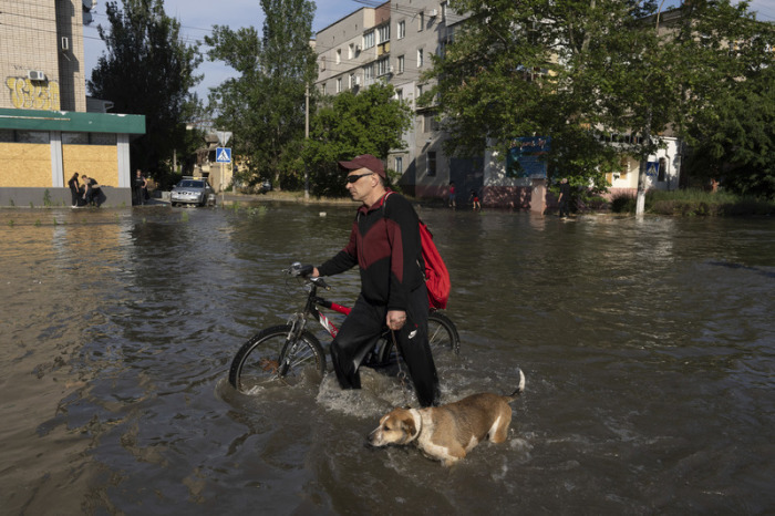 Ein Anwohner mit einem Fahrrad und einem Hund bahnt sich einen Weg durch eine überflutete Straße. Foto: Evgeniy Maloletka/Ap/dpa