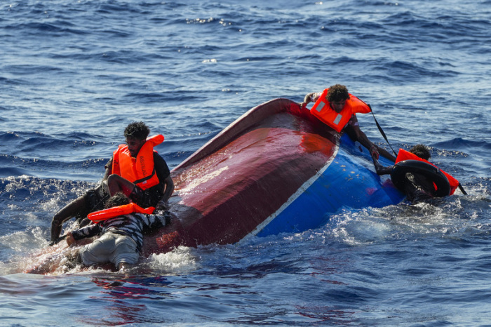 Migranten helfen einander während einer Rettungsaktion der spanischen Nichtregierungsorganisation Open Arms südlich der italienischen Insel Lampedusa im Mittelmeer, auf ihr gekentertes Holzboot zu klettern. Foto: Francisco Seco