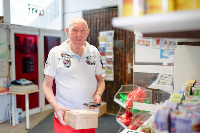 Der 83-jährige Christian Lange hält in seiner Paketannahmestelle ein Paket in den Händen. Foto: Uwe Anspach/dpa