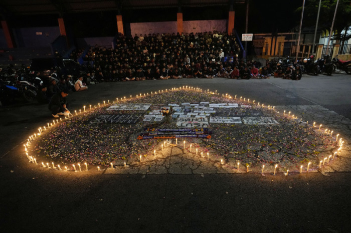 Anhänger des Fußballvereins Arema FC sitzen um ein Herz aus Kerzen herum und beten für die Opfer der tödlichen Massenpanik bei einem Fußballspiel am 01.10.2022. Foto: Achmad Ibrahim/dpa