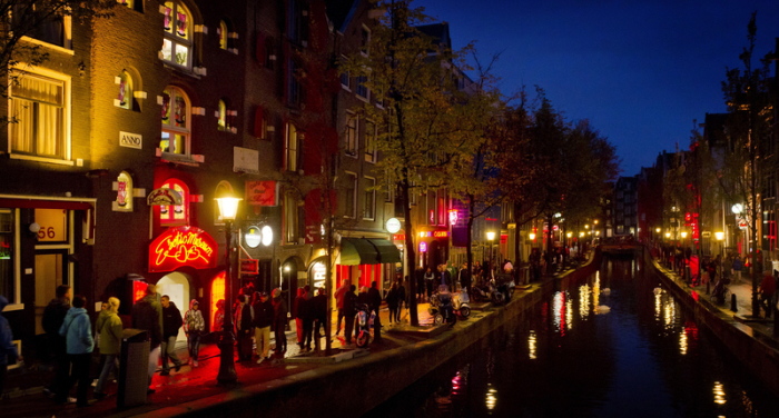enschen schlendern am Abend an einer Gracht entlang durch den Rotlichtbezirk De Wallen. Foto: Koen Van Weel/epa
