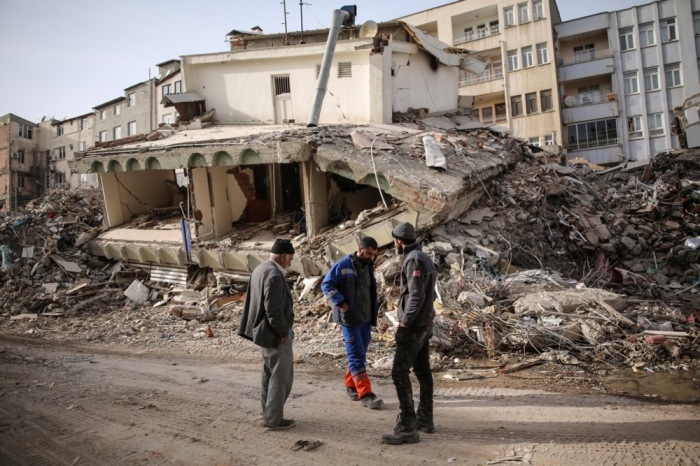 Menschen stehen vor einem eingestürzten Gebäude nach einem starken Erdbeben in Adiyaman. Foto: epa/Str
