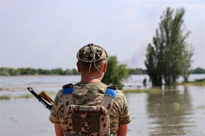 Ein ukrainisches Mitglied der Streitkräfte beobachtet eine Frau, die in einer überfluteten Straße in Kherson steht. Foto: epa/Ivan Antypenko