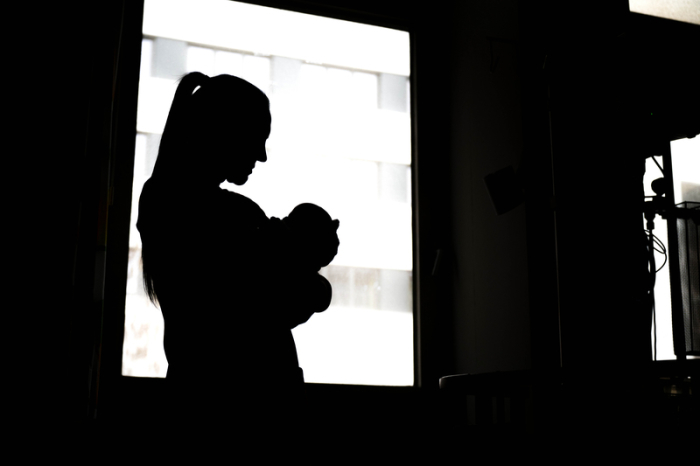 Eine Frau steht mit einem Neugeborenen am Fenster einer Klinik. Foto: Sina Schuldt/dpa