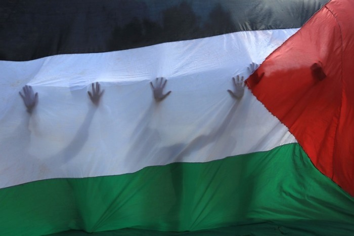 Palästinensische Gebiete, Khan Yunis: Palästinensische Freiwillige stehen hinter einer palästinensischen Fahne, durch die ihre Silhouetten zu erkennen sind. Foto: Ashraf Amra/Apa Images Via Zuma Press Wire/dpa