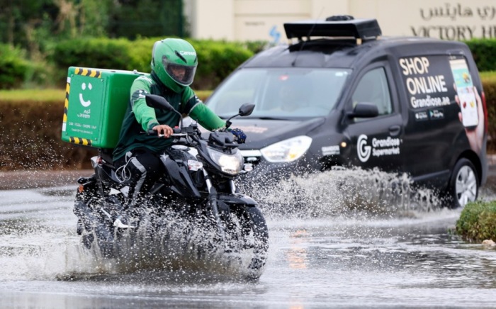Ein Zusteller auf einem Motorrad fährt bei Regen an einem Auto vorbei. Foto: EPA-EFE/Ali Haider