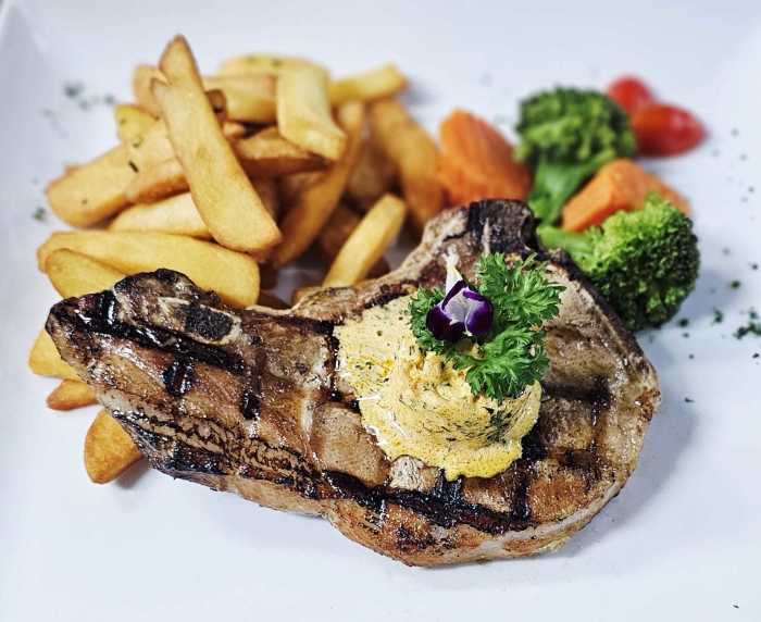 Das gegrillte Schweinskotelett wird mit hausgemachter Kräuterbutter, Pommes frites und Buttergemüse serviert. Bild: Jaybee'Swiss Restaurant