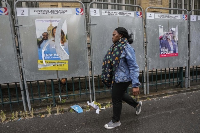 Eine Frau geht an Wahlkampfplakaten für die bevorstehende Parlamentswahl vorbei. (zu dpa: «Hat Macron sich verzockt? Nach Parlamentswahl droht politisches Chaos») Foto: Michel Euler/Ap/dpa