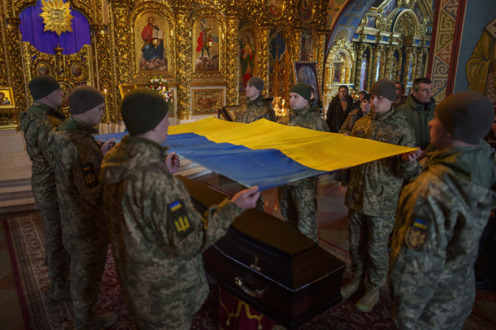 Ukrainische Soldaten halten die Nationalfahne, bevor sie diese auf den Sarg eines gefallenen Soldaten im St. Michaels-Kloster legen. Foto: Vadim Ghirda/Ap/dpa