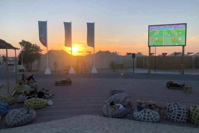 Fußballfans schauen sich im Fan-Dorf in Al-Chaur im Norden von Katar auf einem Großbildschirm ein Spiel der Fußall-WM an. Foto: Jan Kuhlmann/dpa