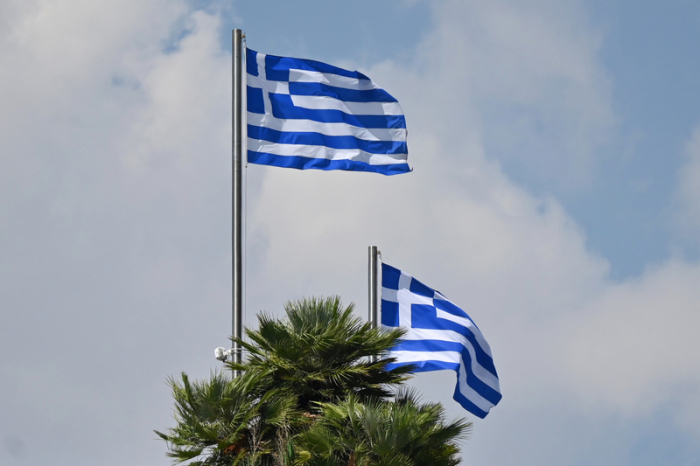 Zwei griechische Nationalflaggen wehen vor einem bewölkten Himmel im Wind. Foto: Anna Ross/dpa
