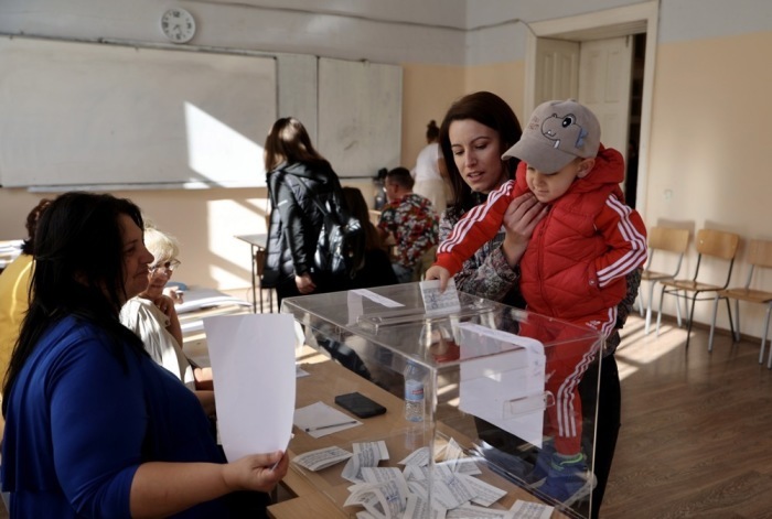 In einem Wahllokal während der Parlamentswahlen in Custendil hält eine Frau ihr Kind, um den Stimmzettel abzugeben. Foto: epa/Georgi Licovski
