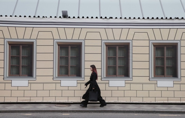 Ein Frau geht auf der Straße vor einem baufälligen Gebäude mit einer Fensterabdeckung in Moskau spazieren. Foto: epa/Yuri Kochetkov
