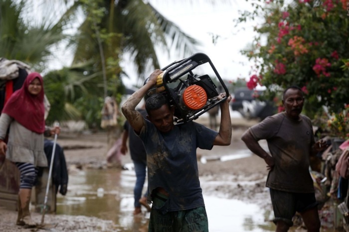 Ein Mann trägt einen Stromgenerator durch schlamm- und wasserbedeckte Straßen in einem überfluteten Dorf in Aceh; Überschwemmungen und Erdrutsche forderten Hunderte Tote. Foto: epa/Hotli Simanjuntak