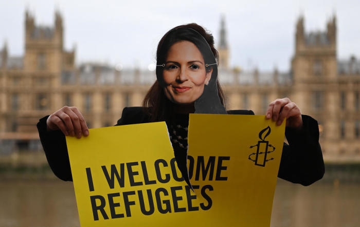 Ein Aktivist von Amnesty International, der eine Maske der britischen Innenministerin Priti Patel trägt, hält ein Plakat während einer 