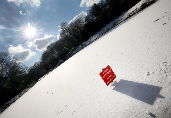 Auf der zugefrorenen Eisfläche eines Teiches im Grugapark ist ein Schild mit der Aufschrift 